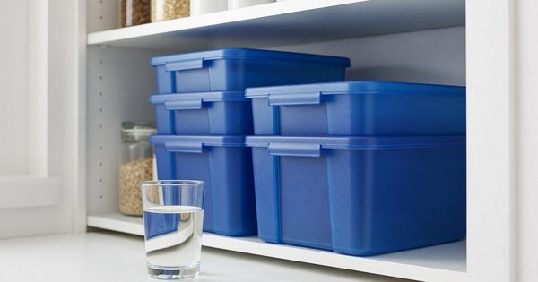 Stacked water storage containers and a filled glass on a pantry shelf